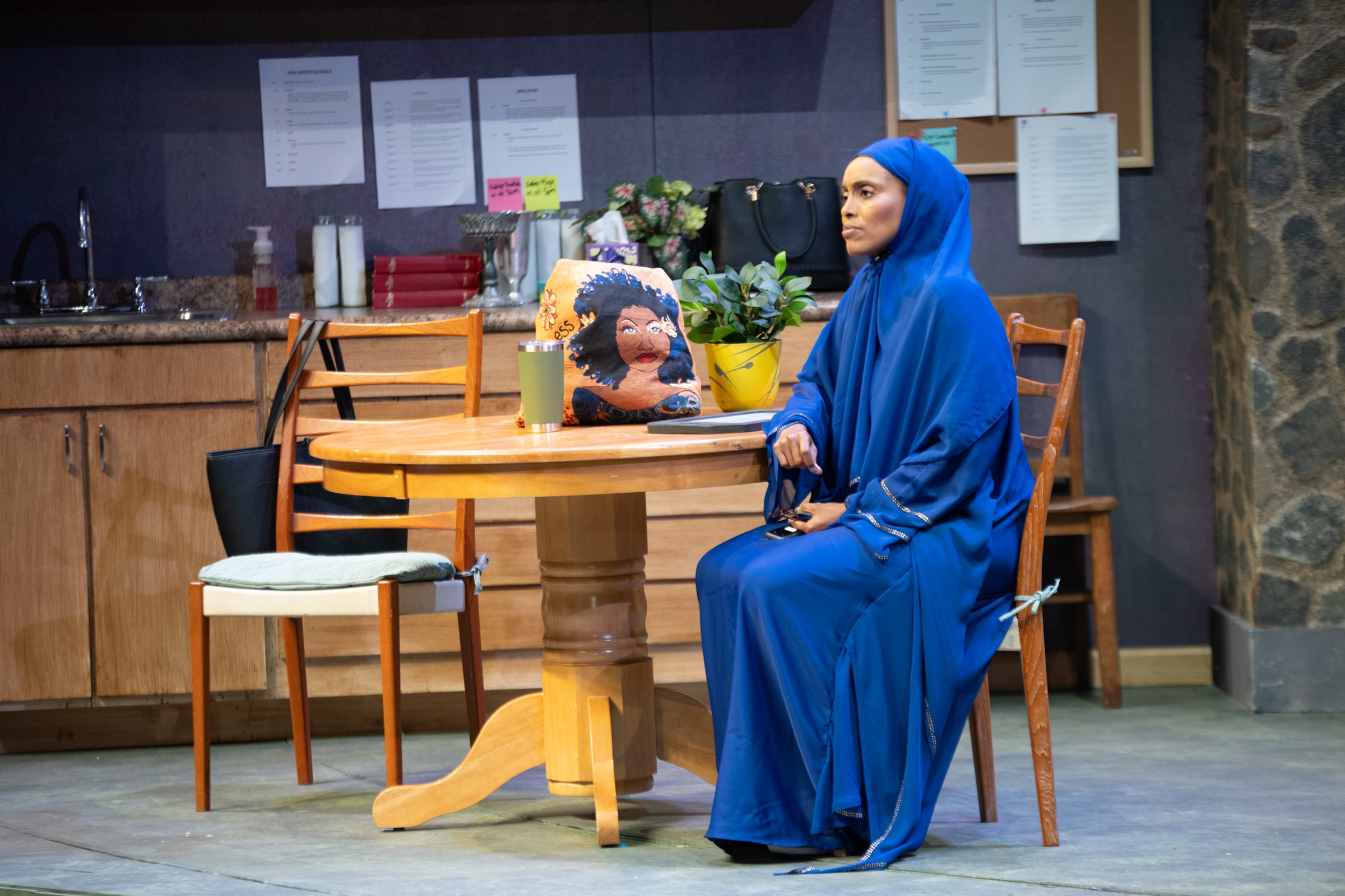 Antu Yacob as Fatima seated at a table in I AM A...SHEPHERDESS by Eljon Wardally